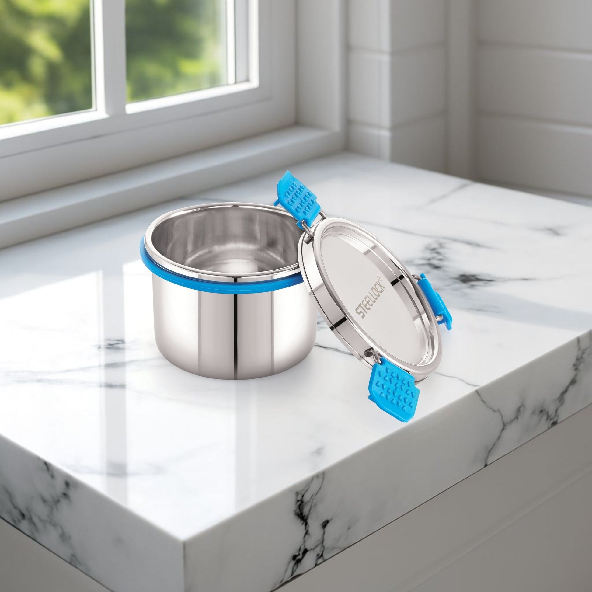 Stainless steel food container with blue straps on a marble surface