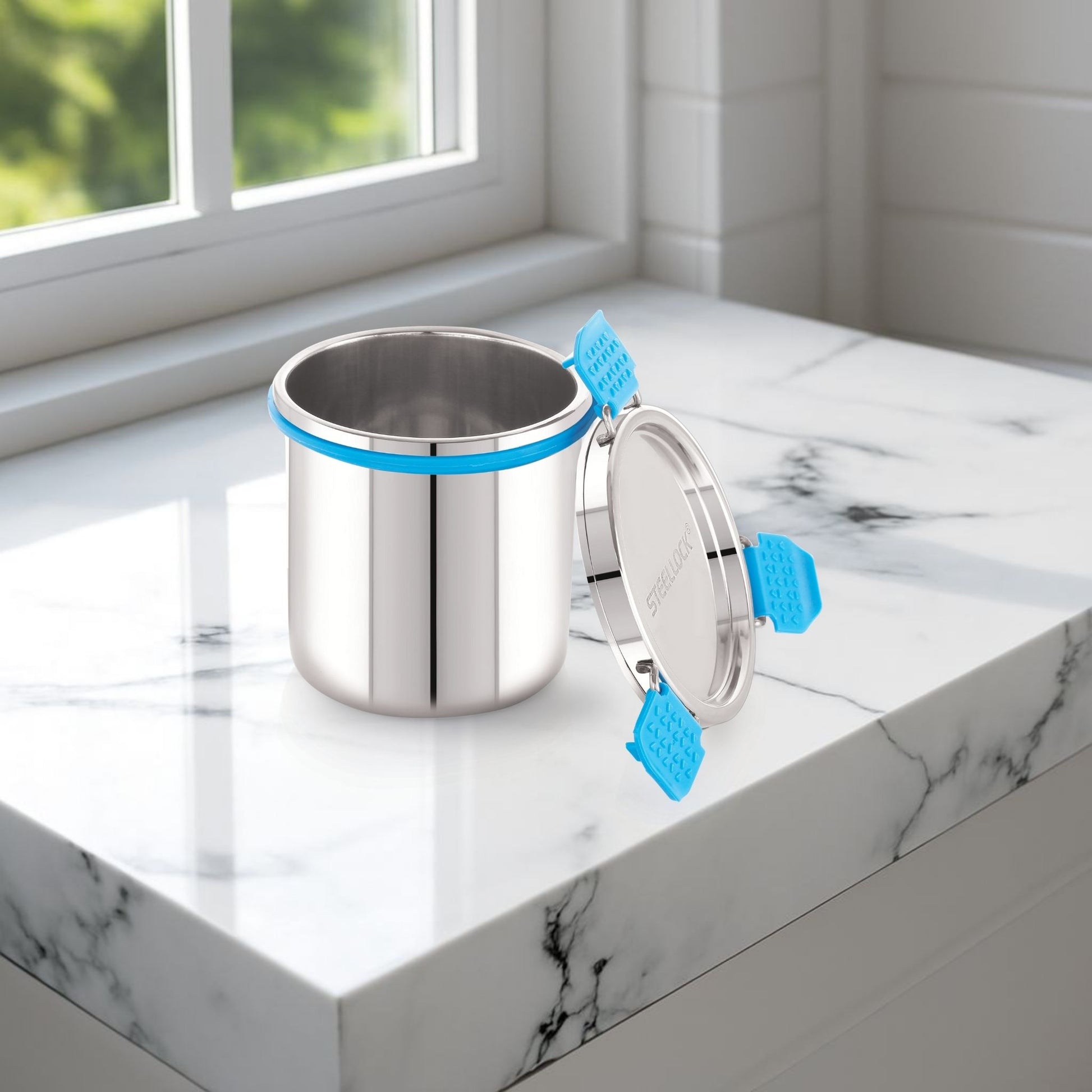 Stainless steel container with blue handles on a marble surface
