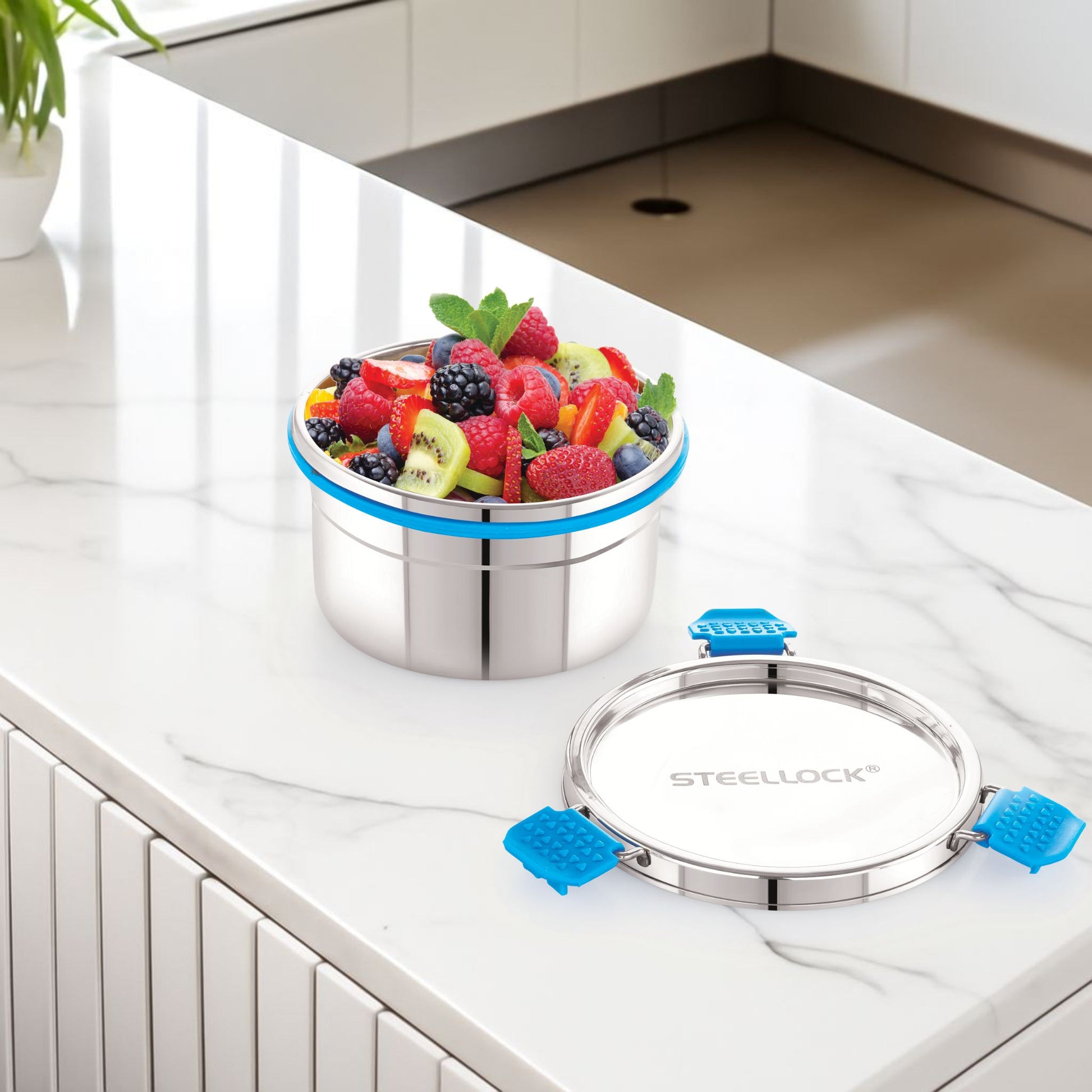 Stainless steel food container with fruits on a kitchen counter, featuring the brand 'SteeLock'.