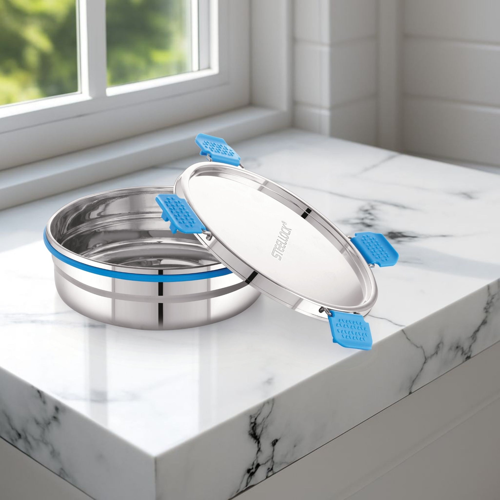 Stainless steel containers with blue silicone seals on a marble surface near a window.